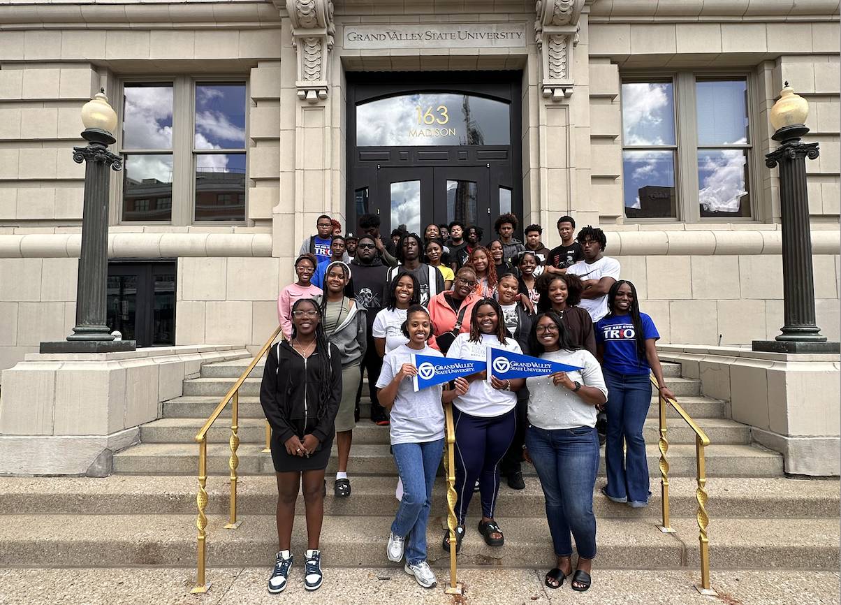 Group photo of students holding GV flags standing in front of GVSU Detroit campus building